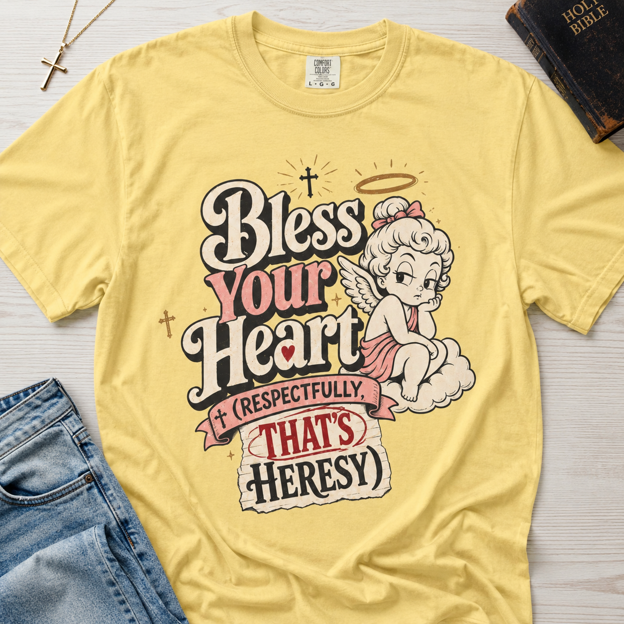 Bless Your Heart Christian humor t-shirt in soft Butter yellow, vintage angel graphic with 'respectfully that's heresy' design.