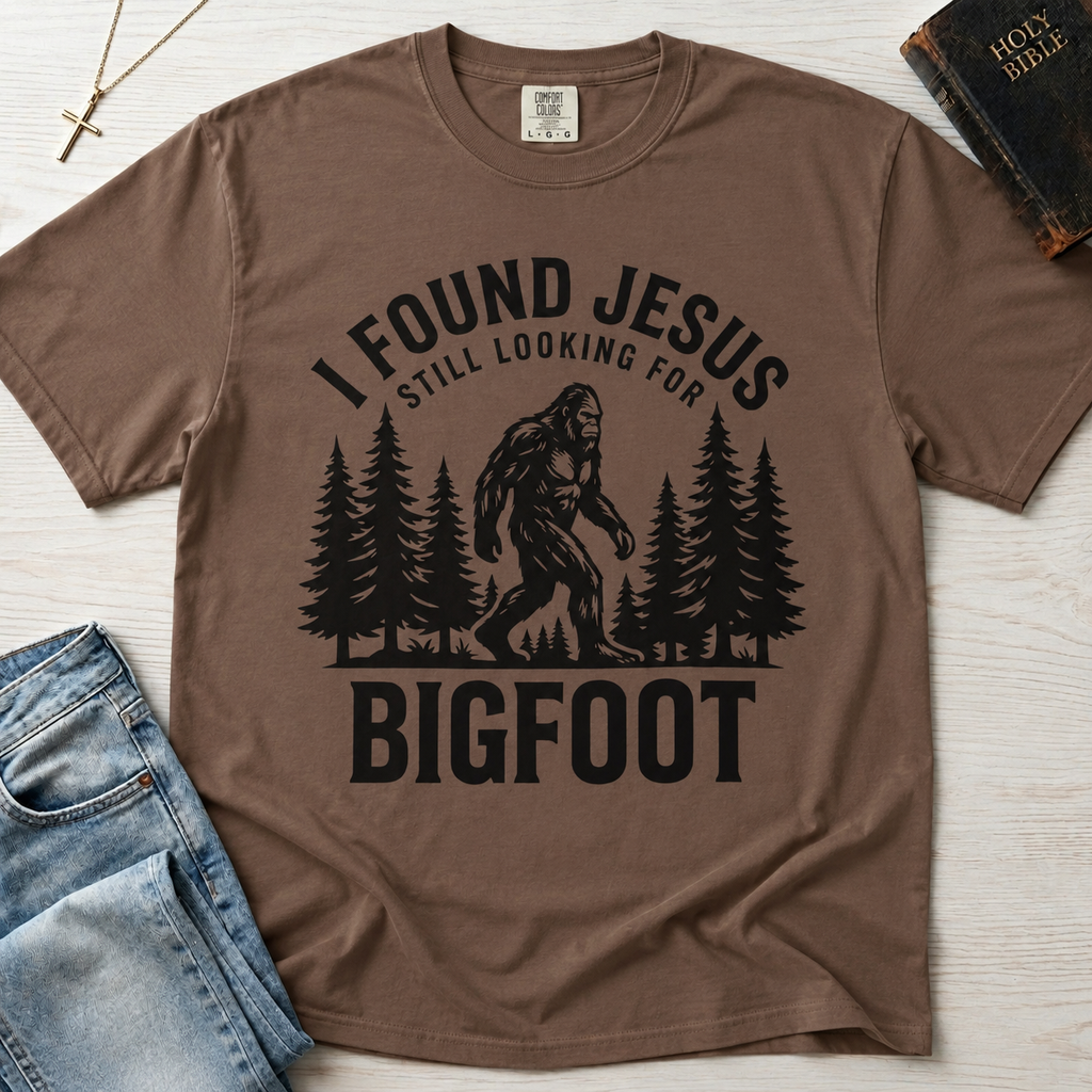 I Found Jesus Still Looking for Bigfoot Christian humor t-shirt in Crunchberry brown, outdoor design with pine trees and sasquatch silhouette.