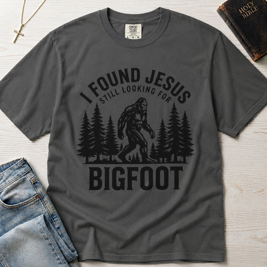 I Found Jesus Still Looking for Bigfoot Christian humor t-shirt in deep Graphite gray, outdoor Bigfoot silhouette with pine forest illustration.