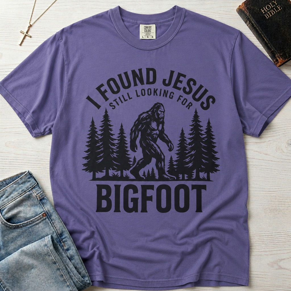 I Found Jesus Still Looking for Bigfoot Christian humor t-shirt in soft Grape purple, outdoor design with Bigfoot and forest silhouettes.