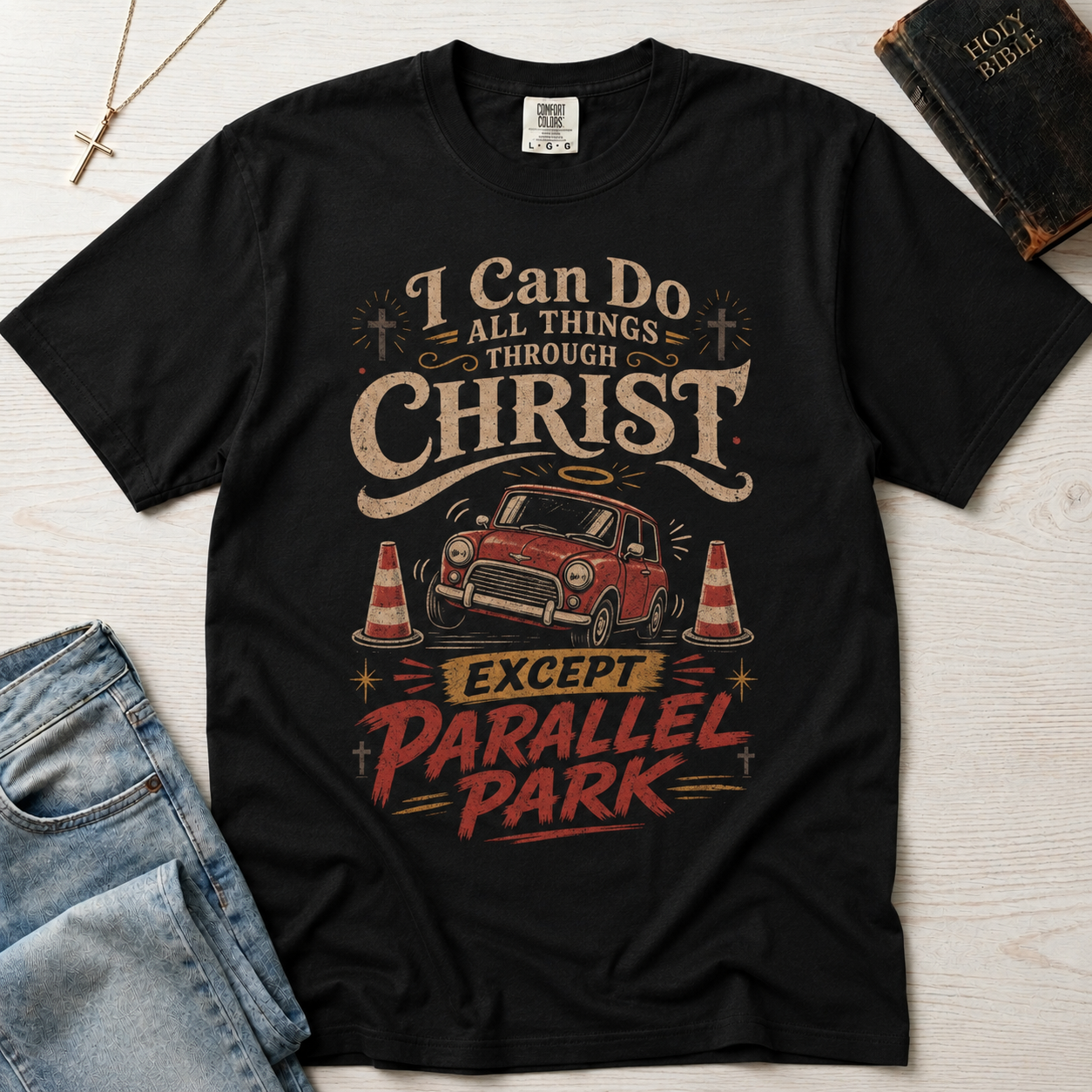 Christian humor t-shirt in black, 'I Can Do All Things Through Christ Except Parallel Park' with vintage truck illustration in orange and white tones.