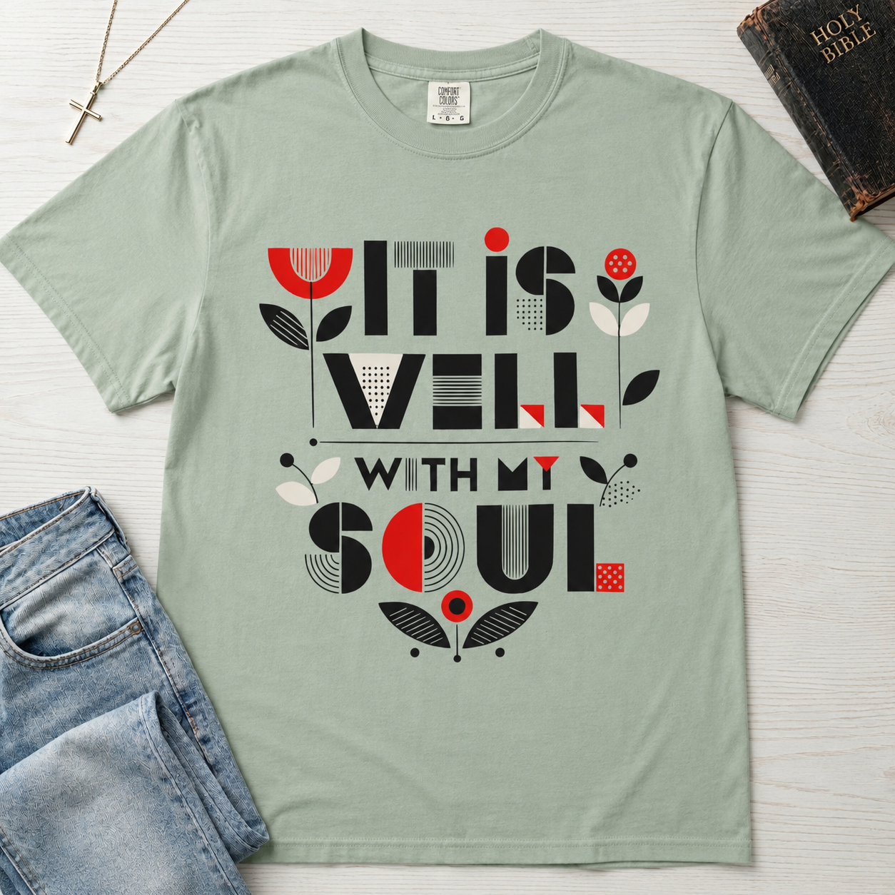 It Is Well With My Soul Christian t-shirt in sage green (Bay); geometric typography with charcoal and coral floral details, garment-dyed cotton.