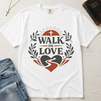 Walk in Love Christian t-shirt in white, garment-dyed cotton tee flat lay with cross necklace and Holy Bible; faith design featuring cross, sunburst and laurel wreath around a heart with winding path.