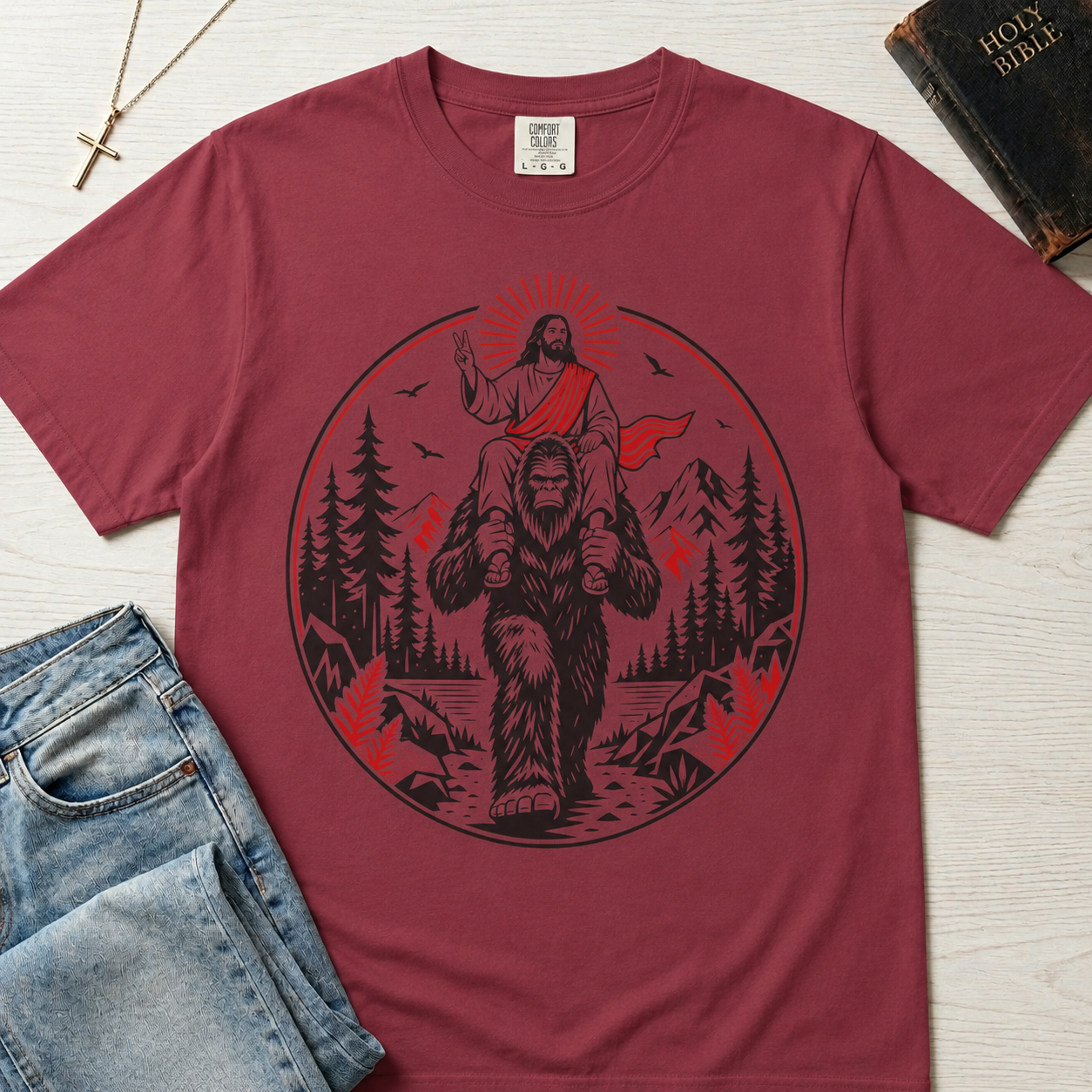 Bigfoot & Jesus Christian t-shirt in dusty rose; circular forest emblem of Jesus riding on Bigfoot's shoulders among pines with a sunburst halo.