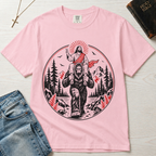 Bigfoot & Jesus Christian t-shirt in light pink; circular forest emblem of Jesus riding on Bigfoot's shoulders among pines with a sunburst halo.