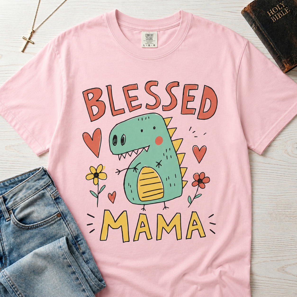 Blessed Mama Dinosaur t-shirt in light pink; cute cartoon green dino among flowers and hearts with 'Blessed Mama' lettering, faith mom tee.