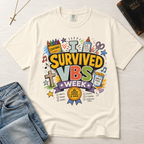 I Survived VBS Week Christian t-shirt in cream ivory; playful graphic with crayons, cross, juice box, stars and an award ribbon, VBS souvenir tee.
